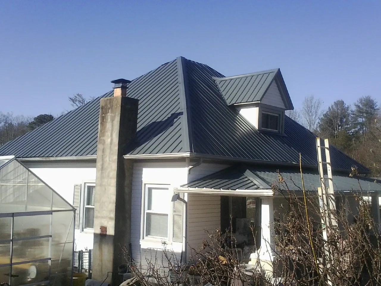 Dark blue standing seam metal roof on a white farmhouse with dormer — Slate & Tile Roof Repair by Roofing Brothers in Hugo