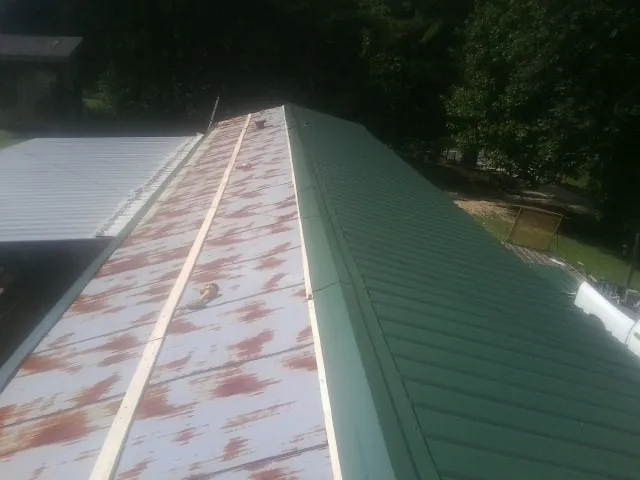 Old rusted panels beside newly installed green metal roofing — Wind Damage Roof Repair by Roofing Brothers in Hugo