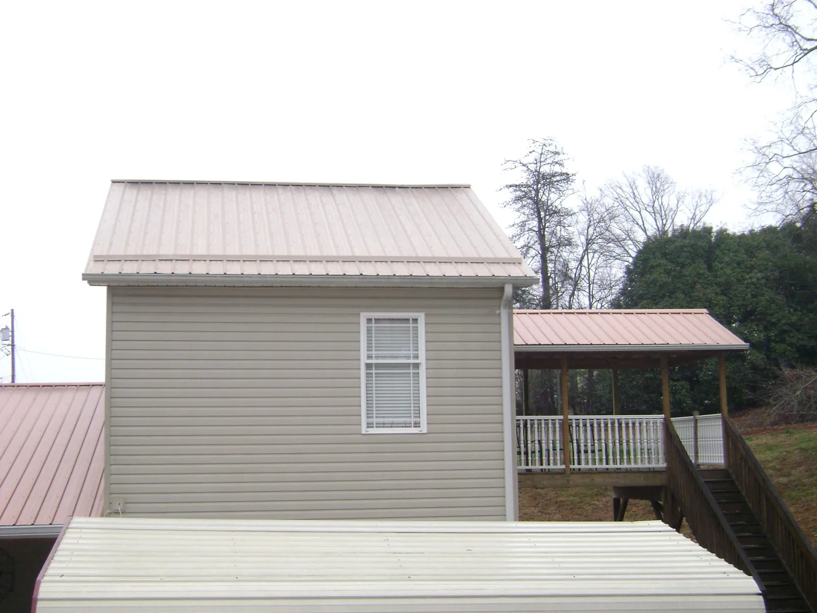 Tan metal roofs on a two story addition and attached porch, from a Roof Replacement job in Hugo